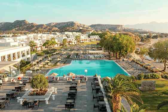 Flyfoto av en ferieanlegg med basseng, solsenger, bygninger og omkringliggende landskap. (AI-generert tekst)