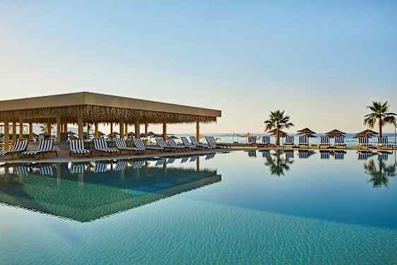 Et utendørs basseng med solsenger og parasoller ved sjøen. (AI-generert tekst)