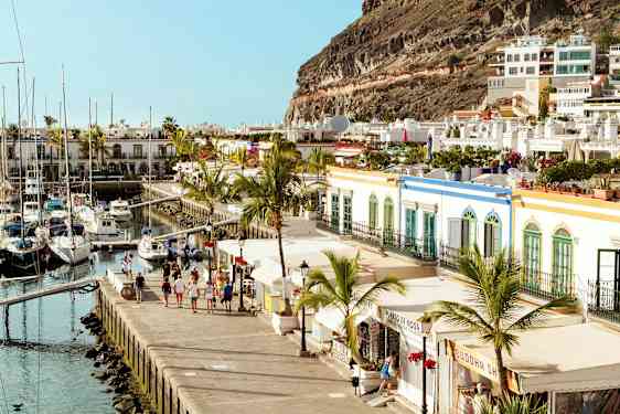 Bilde av en havn med seilbåter, omgitt av fargerike bygninger og palmetrær. (AI-generert tekst)