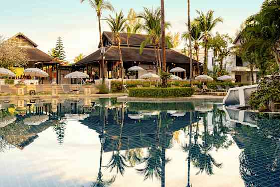 Et utendørsbasseng med solsenger og parasoller ved siden av samt omkringliggende tropisk vegetasjon. (AI-generert tekst)