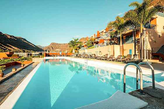 Utendørsbasseng ved et hotell med solsenger og fjell i bakgrunnen. (AI-generert tekst)