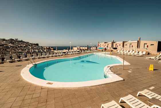 Utsikt over et utendørs svømmebasseng omgitt av solsenger og parasoller. (AI-generert tekst)