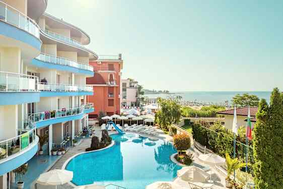 Bilde av et hotell ved havet med basseng og omkringliggende grøntområder. (AI-generert tekst)