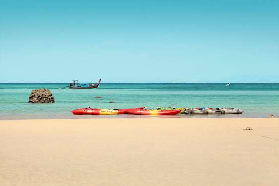 Flere kajakker på en sandstrand, med havet og en båt i bakgrunnen. (AI-generert tekst)