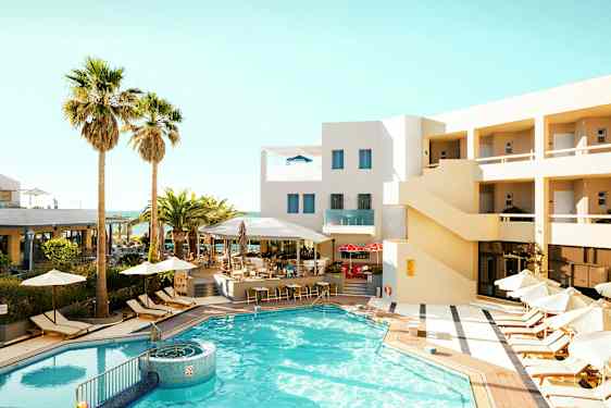 Et utendørs basseng omgitt av solsenger og parasoller ved et hotell med beige fasade. (AI-generert tekst)