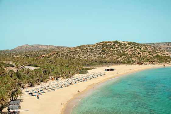 Sandstrand med turkis hav, solsenger og parasoller. Bakgrunn med vegeterte fjell. (AI-generert tekst)