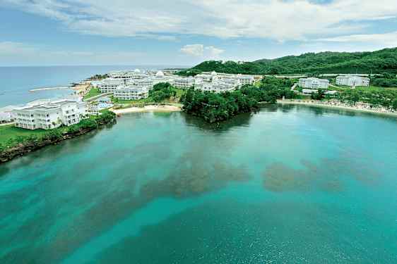 Bilde av en kyst med klart vann og hvite bygninger omgitt av grøntområder. (AI-generert tekst)