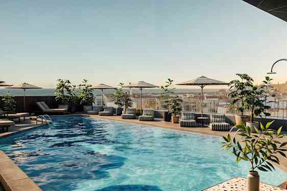 Utendørsbasseng med parasoller, solsenger og planter rundt. (AI-generert tekst)