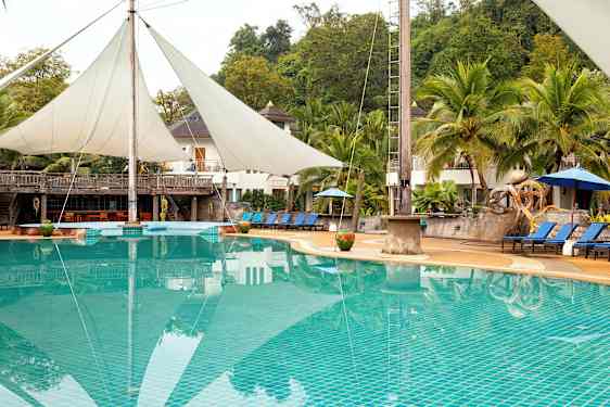 Et basseng med solsenger og parasoller, omgitt av palmetrær og bygninger i bakgrunnen. (AI-generert tekst)