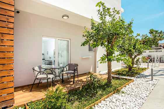 En terrasse med tregulv og to stoler rundt et bord, omringet av planter og et sitrustre. (AI-generert tekst)