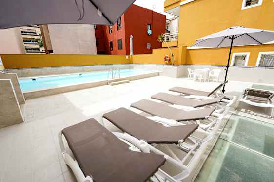 Utendørs basseng med solsenger og parasoller på et steinlagt område. (AI-generert tekst)