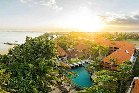 Et utendørsbilde av et tropisk hotellområde med basseng og havet i bakgrunnen ved soloppgang. (AI-generert tekst)