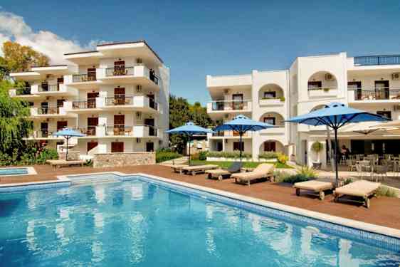 Hvit bygning med balkonger, basseng og solsenger med blå parasoller. (AI-generert tekst)