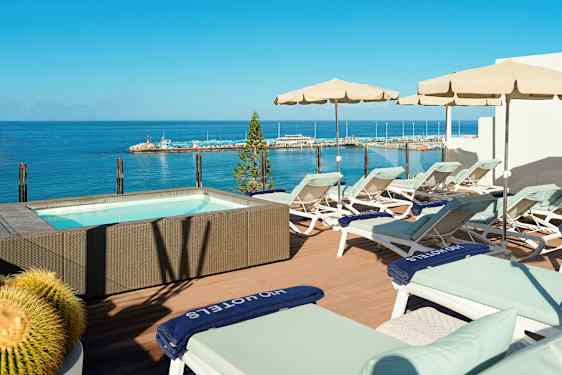 Terrasse med solsenger og parasoller ved et boblebad med havutsikt. (AI-generert tekst)