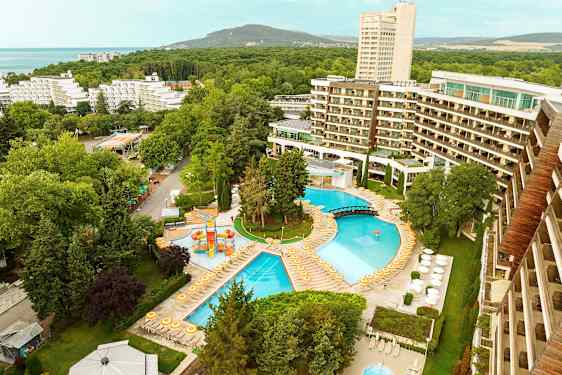 Utsikt over et hotellområde med bassenger, solsenger og omkringliggende trær. (AI-generert tekst)