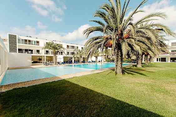 Hotellbygning ved et utendørs basseng, omgitt av palmetrær og gressplen. (AI-generert tekst)