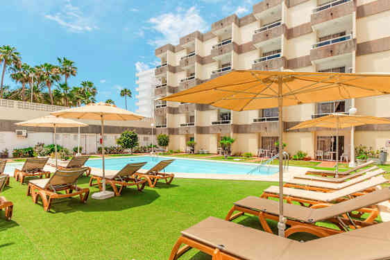Utendørsområde med solsenger, parasoller og basseng foran et hotell. (AI-generert tekst)