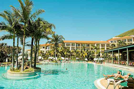 Oppvarmet utendørsbasseng omgitt av palmer ved hotell med flere etasjer. (AI-generert tekst)