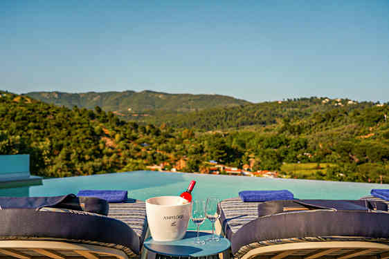 Solstoler ved et infinitybasseng med panoramautsikt over grønne fjell og åser. (AI-generert tekst)