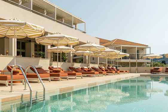 Et basseng omgitt av solsenger og parasoller ved en bygning. (AI-generert tekst)