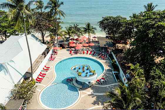 Luftfoto av et basseng på et feriested med solsenger og parasoller, omgitt av tropiske trær og nær havet. (AI-generert tekst)