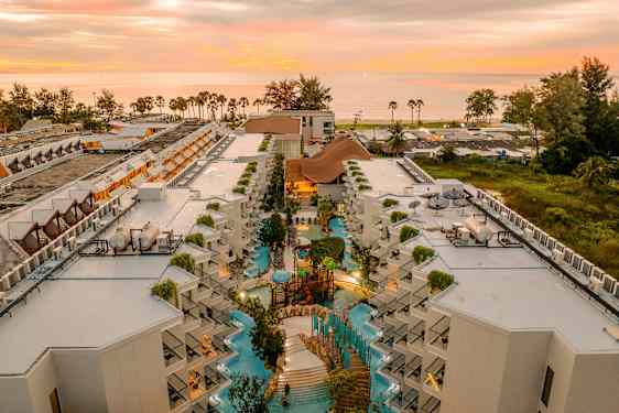 Luftfoto av hotellkompleks med bassengområde og solnedgang i bakgrunnen. (AI-generert tekst)