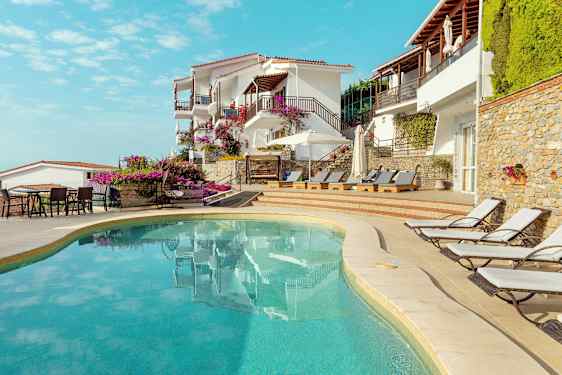 Utendørsbasseng ved hotell bygget i middelhavsstil med solsenger og blomster. (AI-generert tekst)