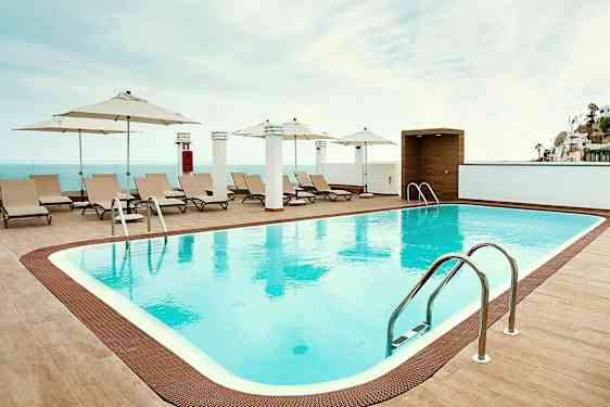 Et utendørs svømmebasseng med solsenger og parasoller langs kanten. (AI-generert tekst)