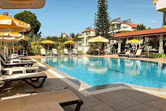 Et utendørs svømmebasseng med solsenger og parasoller, omgitt av grøntområder og bygninger. (AI-generert tekst)