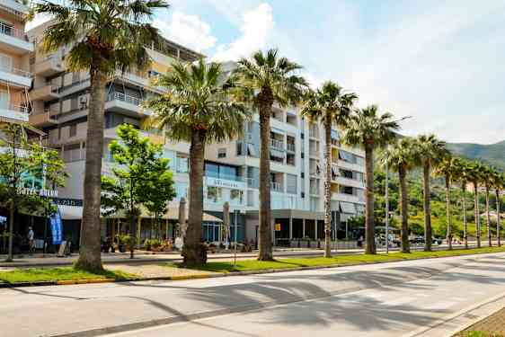 Leilighetsbygninger med palmer og grøntområde langs en bred vei. (AI-generert tekst)