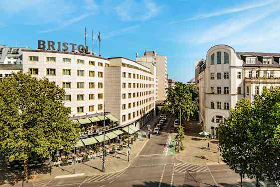 Et bylandskap som viser en bygning med teksten "Bristol" på taket, omgitt av trær og en gate med uteservering. (AI-generert tekst)