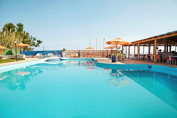 Et utendørs svømmebasseng med parasoller og bord ved siden av. (AI-generert tekst)