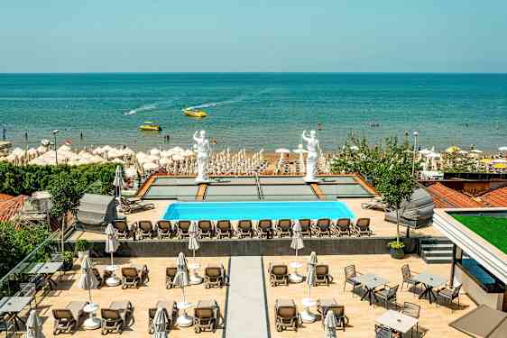 Utsikt over et basseng med solsenger, statuer og en sandstrand ved sjøen. (AI-generert tekst)