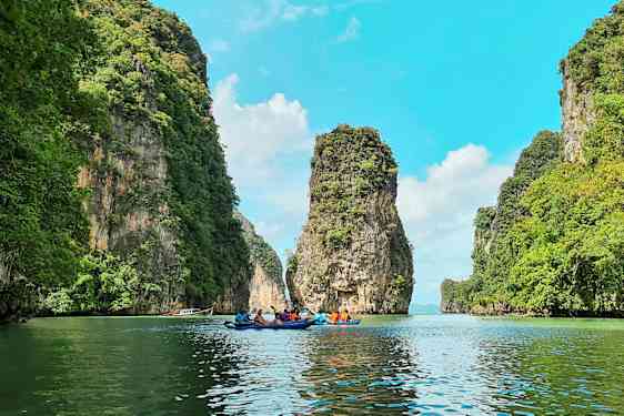 Flere personer padler kajakker gjennom en naturskjønn passasje mellom høye, grønne klipper. (AI-generert tekst)