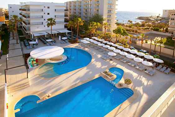 Hotellområde nær sjøen med basseng, solsenger og parasoller. (AI-generert tekst)