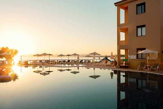 Et bassengområde ved en bygning med utsikt over havet under en solnedgang. (AI-generert tekst)