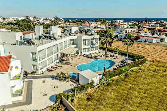 Flyfoto av hotellområde med basseng og omkringliggende bygninger. (AI-generert tekst)