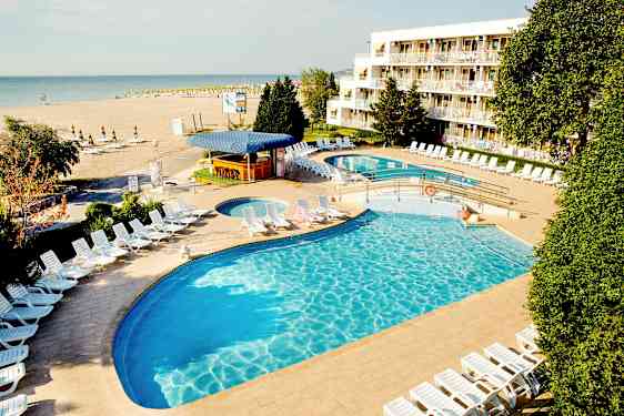 Et hotellbasseng med solsenger og en strand i bakgrunnen. (AI-generert tekst)