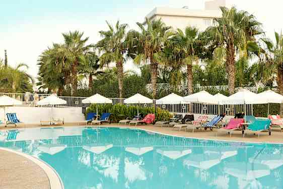 Utendørsbasseng med solsenger og parasoller omgitt av palmer. (AI-generert tekst)