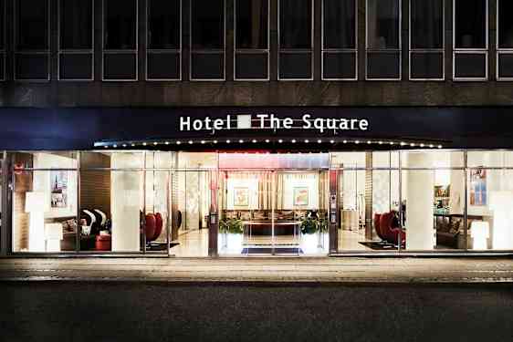 Fasaden og hovedinngangen til Hotel The Square, med glassdører og store vinduer. (AI-generert tekst)