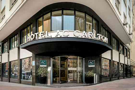 En hotellfasade med skilteteksten "HOTEL AC CARLTON" synlig over inngangen. (AI-generert tekst)