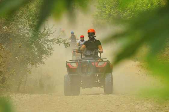 Personer som kjører firehjulinger på en støvete grusvei omgitt av vegetasjon. (AI-generert tekst)