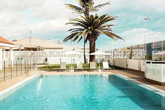 Utendørsbasseng med solsenger og parasoller samt en palme i bakgrunnen. (AI-generert tekst)