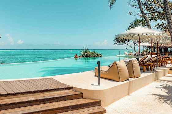 Et evighetsbasseng ved havet, omgitt av solsenger og parasoller. (AI-generert tekst)