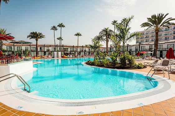 Utendørsbasseng omgitt av solsenger og palmer ved et hotell. (AI-generert tekst)