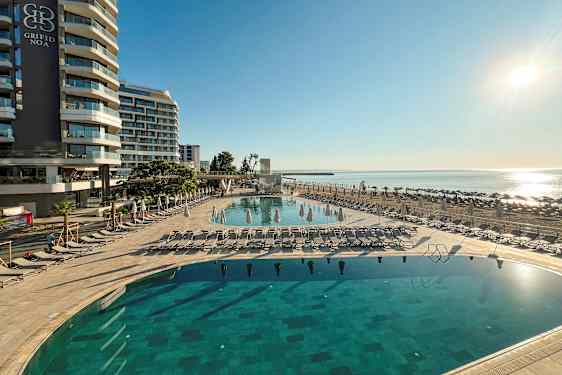 Hotellbygning ved strandpromenade med basseng og solsenger. (AI-generert tekst)