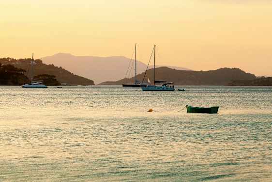 Bilde av en rolig vik ved solnedgang med seilbåter og en grønn båt i forgrunnen. (AI-generert tekst)