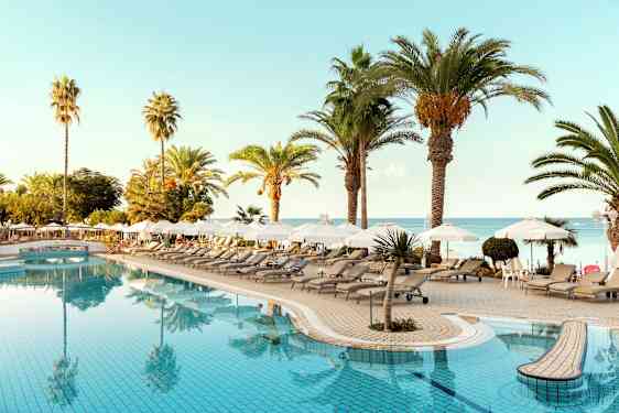 Bassengområde med solsenger, parasoller og palmer nær havet. (AI-generert tekst)