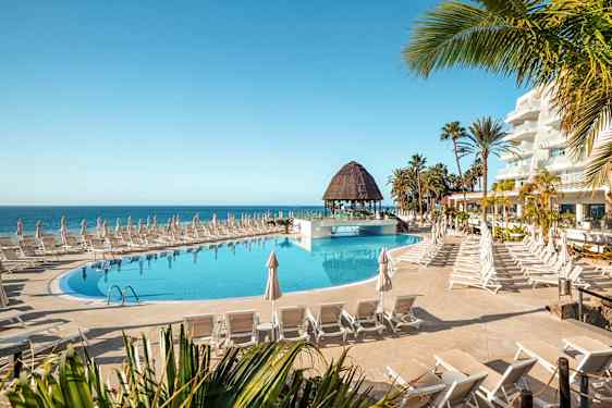 Bassengområde med solsenger og parasoller nær sjøen. (AI-generert tekst)