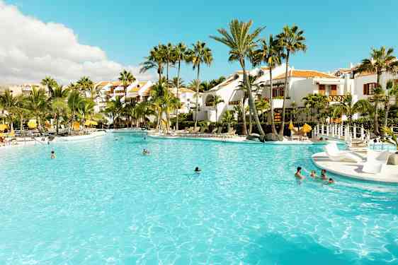 Stor basseng omgitt av palmer og hvite bygninger. (AI-generert tekst)